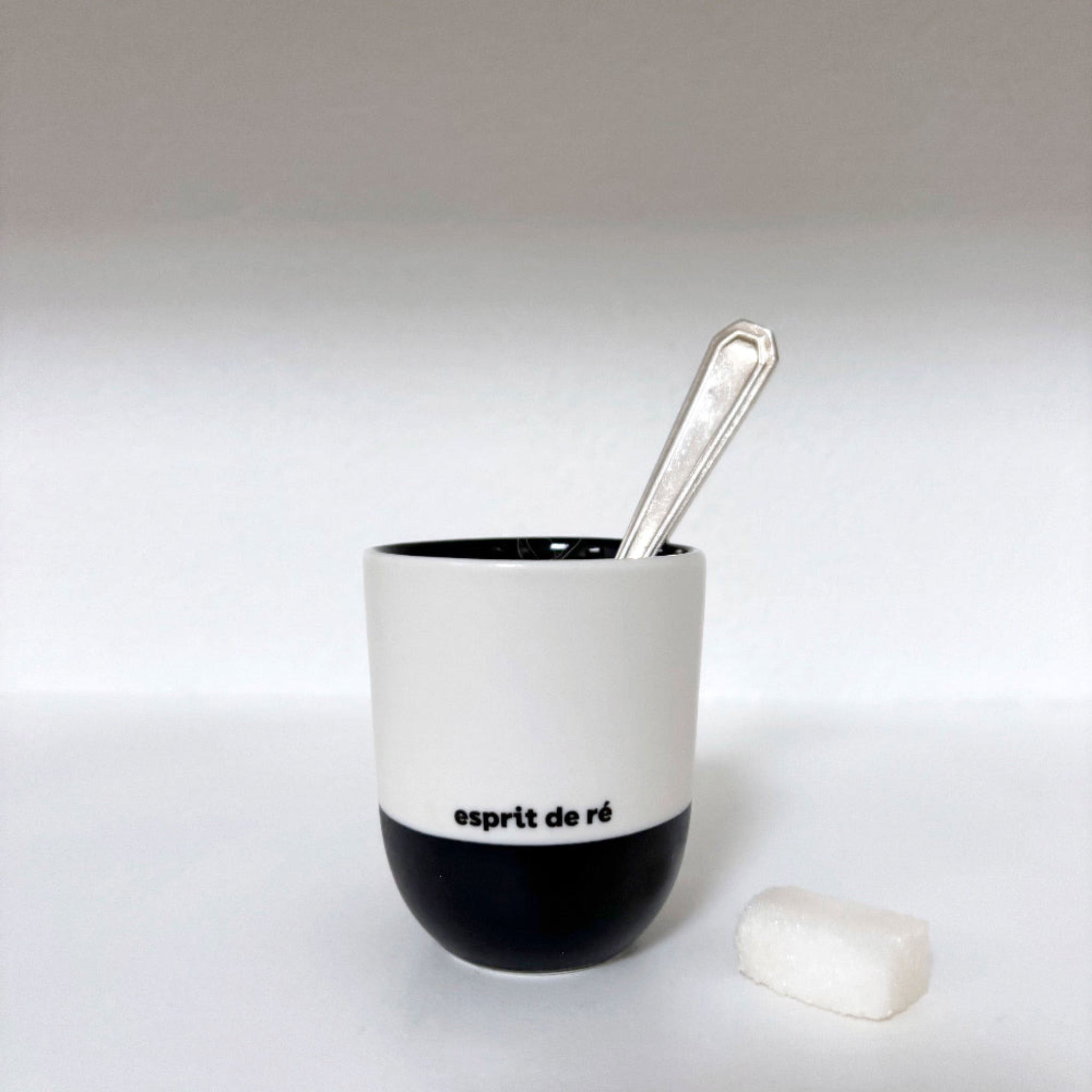 White and black ceramic cup with a spoon on a light gray background